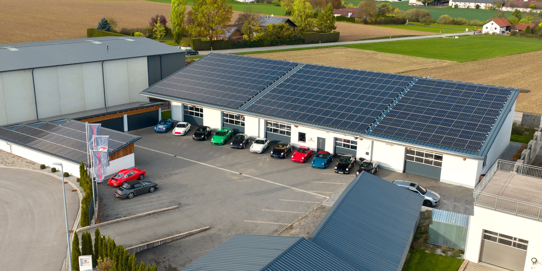 Luftbild der Paintmayer Motorenmanufaktur in der Boschstraße in Massing mit Porsche-Fahrzeugen vor der Halle