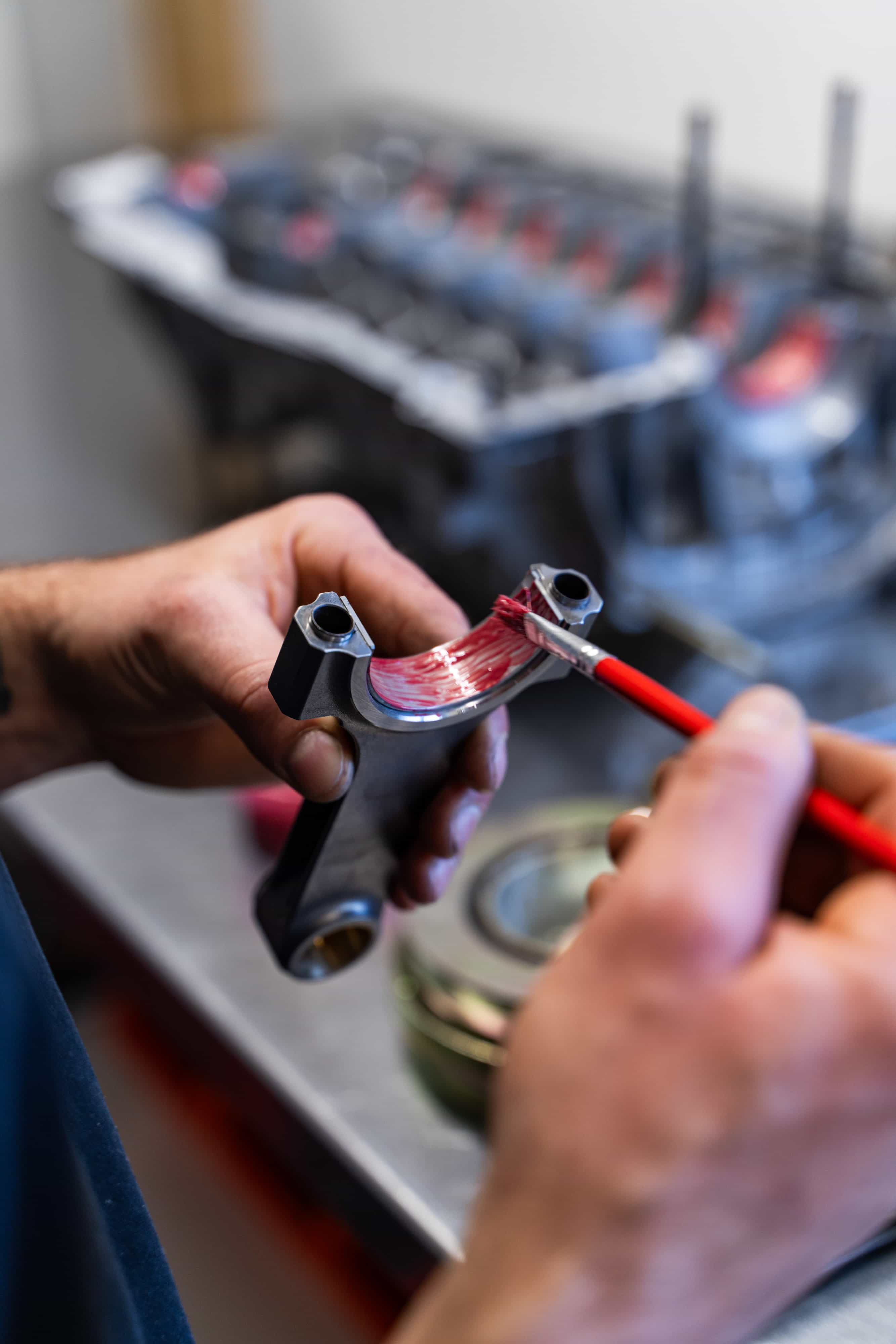 paintmayer_manufaktur_porsche_137©invisions.at Eine CNC-Fräsmaschine in Betrieb, die ein in einem Schraubstock befestigtes Metallwerkstück zerspant, wobei Metallspäne und Kühlmittel auf dem Maschinenbett sichtbar sind.