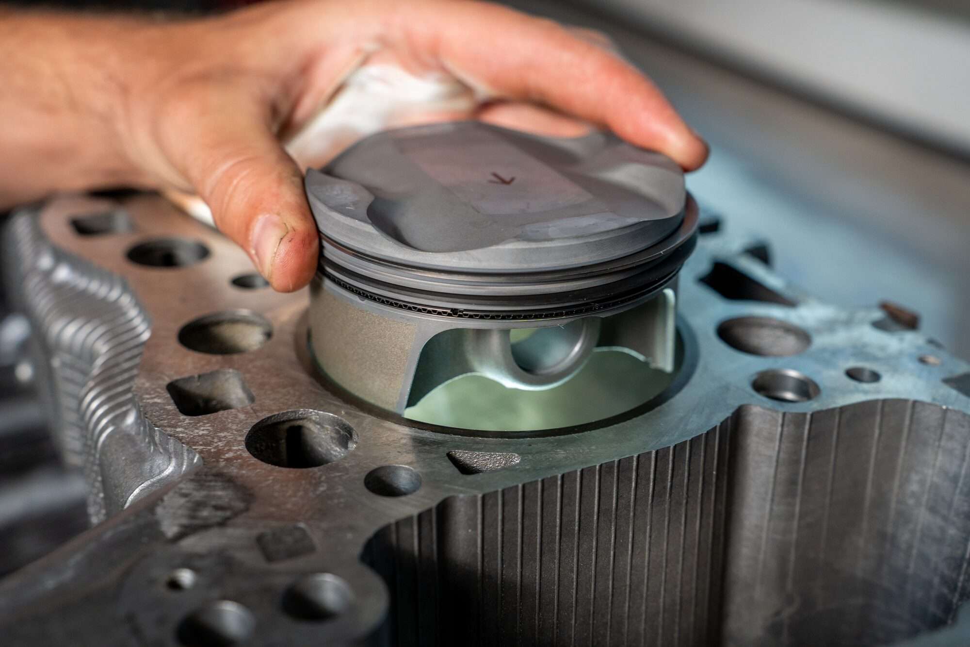 Mechaniker setzt Kolben in den verrippten Zylinder eines Porsche-Motorblocks beim Motorenbau Paintmayer ein